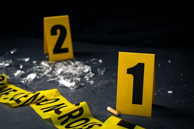 Photo of Broken bottle, yellow tape and evidence markers on black slate table, closeup. Crime scene