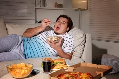 Overweight man with bowl of popcorn on sofa at home