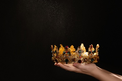 Woman holding beautiful golden crown on black background, closeup with space for text. Fantasy item