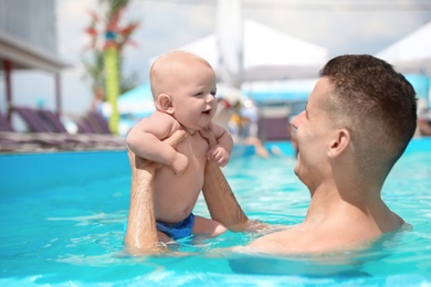 Man with his little baby in swimming pool on sunny day, outdoors