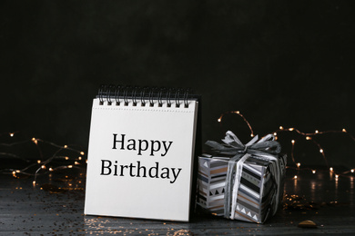 Notepad with greeting HAPPY BIRTHDAY and gift on wooden table