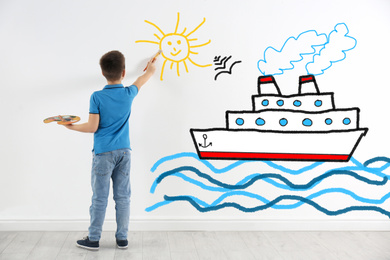 Cute child drawing sea with cruise ship on white wall indoors