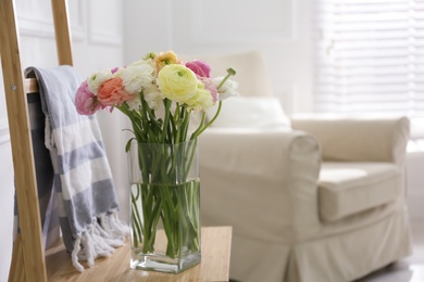 Beautiful ranunculus flowers in vase on wooden chair indoors, space for text