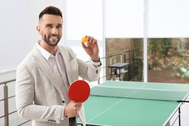 Businessman with tennis racket and ball near ping pong table in office. Space for text