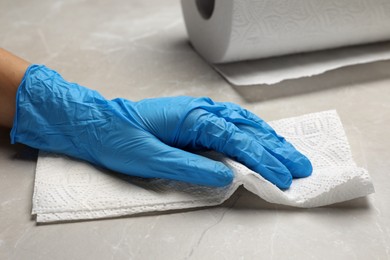 Woman in glove cleaning light grey table with paper towel, closeup