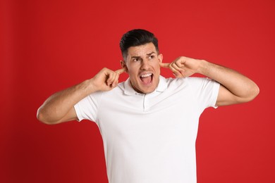 Emotional man covering ears with fingers on red background