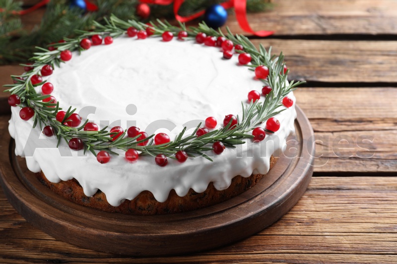Photo of Traditional Christmas cake decorated with rosemary and cranberries on wooden table, closeup
