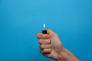 Woman holding lighter on light blue background, closeup. Space for text