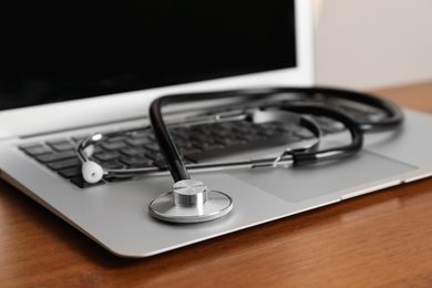Modern laptop with stethoscope on wooden table, closeup