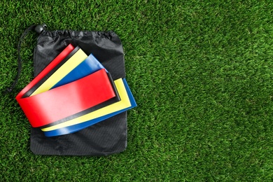 Photo of Bag with fitness elastic bands on green grass, top view. Space for text
