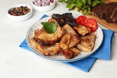 Photo of Tasty fried pork lard with parsley and tomatoes on white wooden table