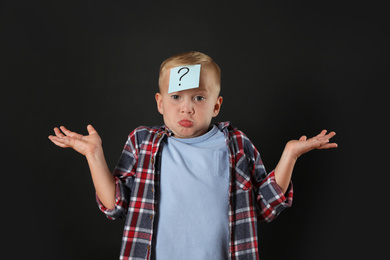 Photo of Confused boy with question mark sticker on forehead against black background