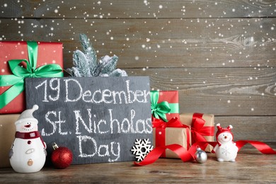 Board with text 19 December St. Nicholas Day, gift boxes and festive decor on wooden table