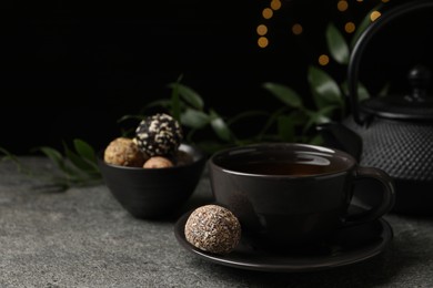 Cup of aromatic tea and delicious vegan candy balls on grey table against blurred lights, space for text