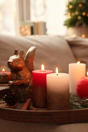 Tray with beautiful burning candles and Christmas decor on sofa at home, closeup