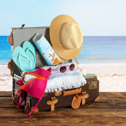 Open vintage suitcase packed for summer vacation on wooden surface against sandy beach