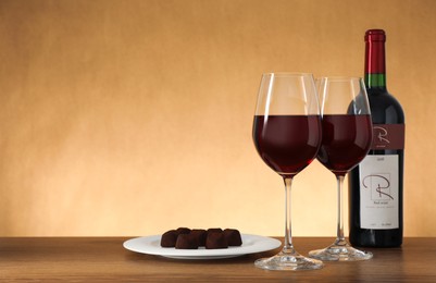 Bottle and glasses of red wine with chocolate candies on wooden table. Space for text
