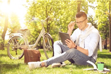 Image of Man working with tablet in park near bicycle on sunny day