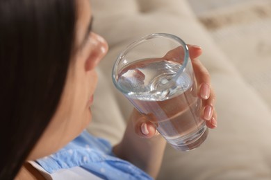 Young woman drinking water on sofa, closeup. Refreshing drink