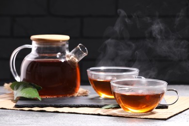 Photo of Aromatic hot tea in glass cups and teapot on light grey table near brick wall