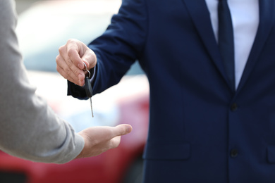 Salesman giving key to customer in modern auto dealership, closeup. Buying new car