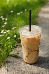 Photo of Takeaway plastic cup with cold coffee drink and straw near green grass outdoors