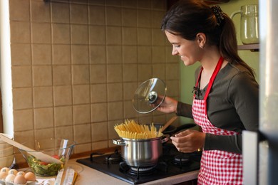Young woman cooking spaghetti on stove in kitchen