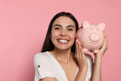 Photo of Emotional young woman with ceramic piggy bank on pale pink background