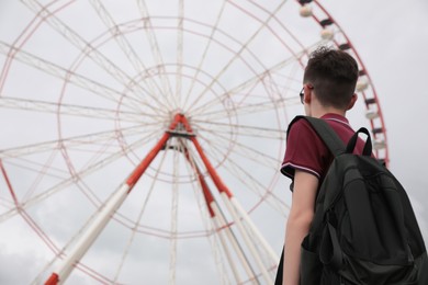 Teenage boy near large Ferris wheel outdoors, back view. Space for text