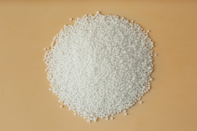Pellets of ammonium nitrate on beige background, flat lay. Mineral fertilizer
