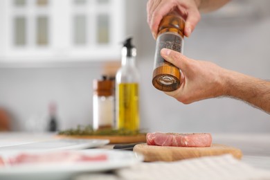 Photo of Man peppering steak at table in kitchen, closeup. Online cooking course