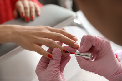 Professional manicurist applying polish on client's nails in beauty salon, closeup