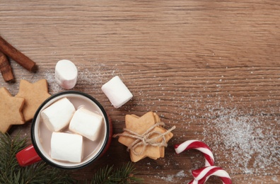Flat lay composition with marshmallows, hot drink and sweets on wooden table. Space for text
