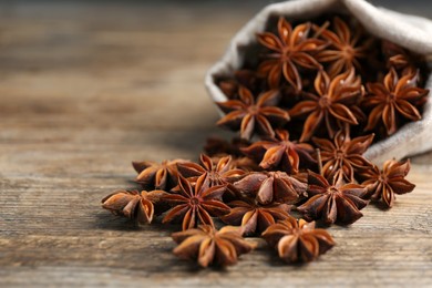 Photo of Overturned bag with aromatic anise stars on wooden table, closeup. Space for text