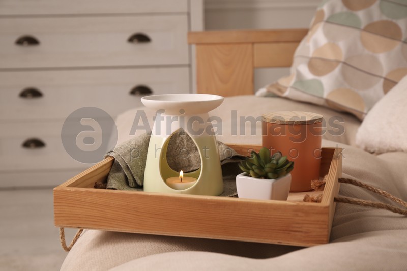 Tray with stylish aroma lamp and houseplant on sofa in room