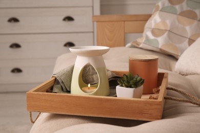 Tray with stylish aroma lamp and houseplant on sofa in room