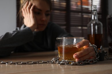 Alcohol addiction. Woman chained with glass of liquor at wooden table in room, focus on hand