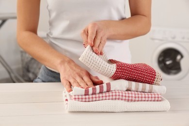 Photo of Woman with clean kitchen towels at white wooden table in laundry room, closeup