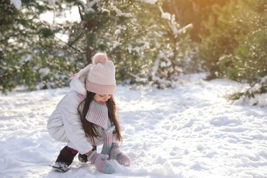 Cute little girl rolling snowball in winter forest