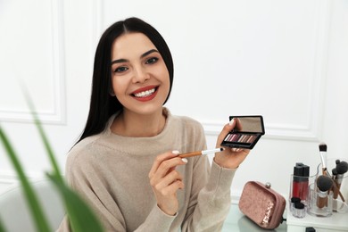 Beautiful happy woman applying makeup in room
