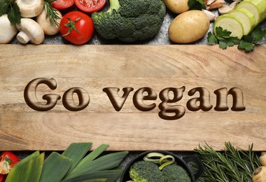 Wooden board with phrase Go Vegan and fresh vegetables on table, flat lay