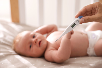 Photo of Cute baby lying in crib, focus on woman holding digital thermometer. Health care