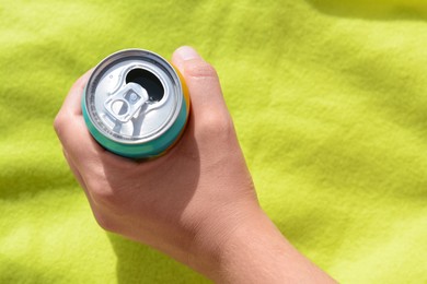 Woman holding aluminum can with beverage on yellow blanket, top view. Space for text