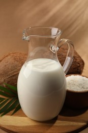 Photo of Glass jug of delicious vegan milk near coconuts on brown background