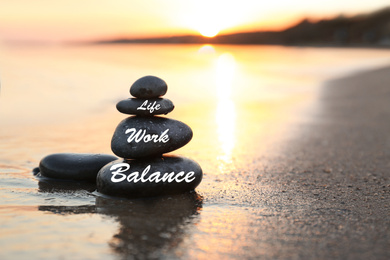 Work-life balance concept. Stacked stones on sandy beach at sunset, space for text