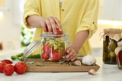Woman putting tomatoes into pickling jar at kitchen table, closeup