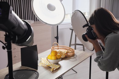 Young woman with professional camera taking photo of lemons in studio