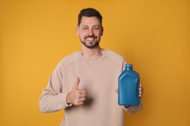 Man holding blue container of motor oil and showing thumbs up on orange background