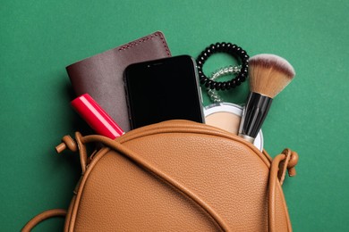 Photo of Stylish woman's bag with smartphone and accessories on green background, flat lay