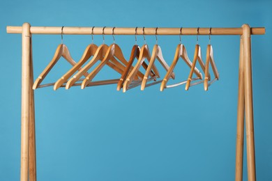 Photo of Empty clothes hangers on wooden rack against light blue background